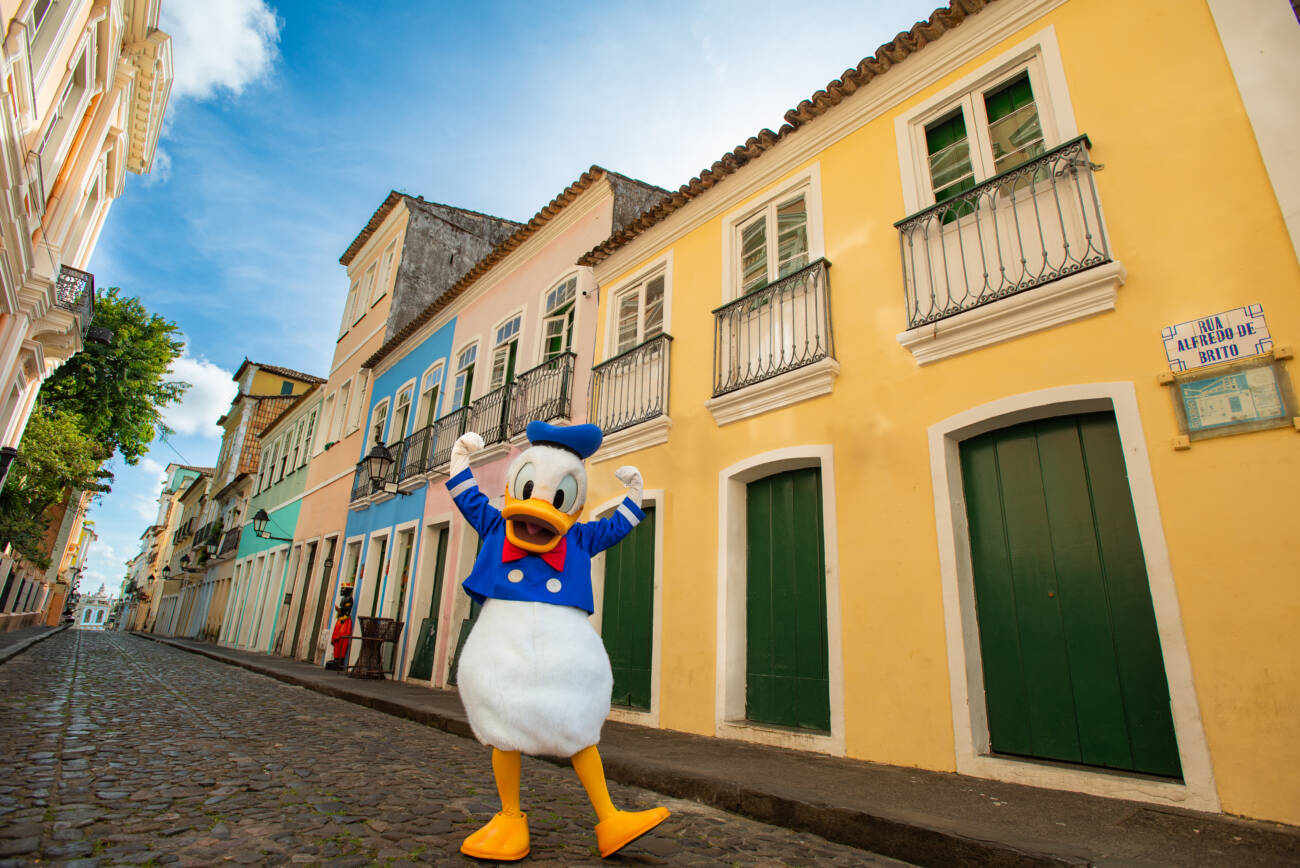 Personagem em rua histórica com casas coloridas.