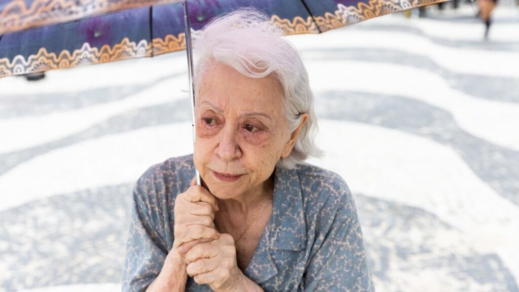 Idosa com guarda-chuva na calçada de mosaico.