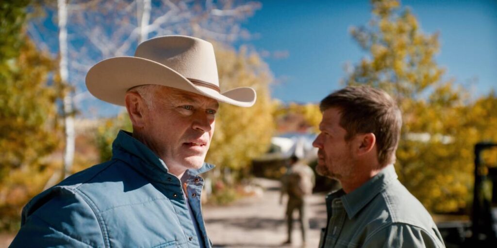 Dois homens conversam ao ar livre, um usando chapéu cowboy.